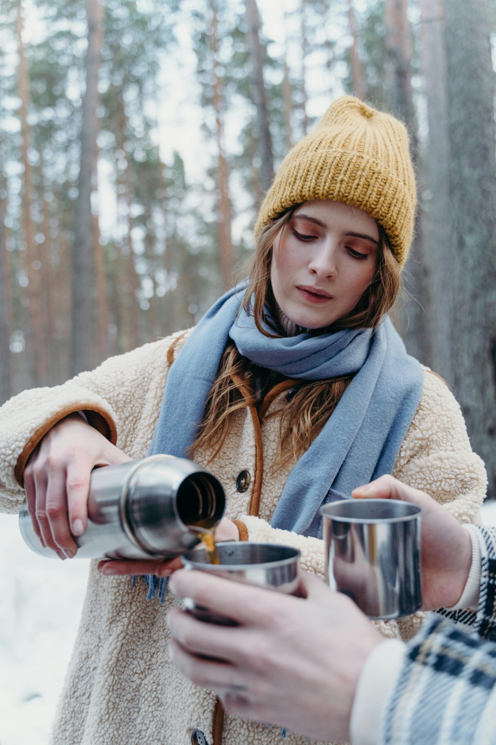 Frau schenkt mit Thermosflasche ein. Schnee im Wald.