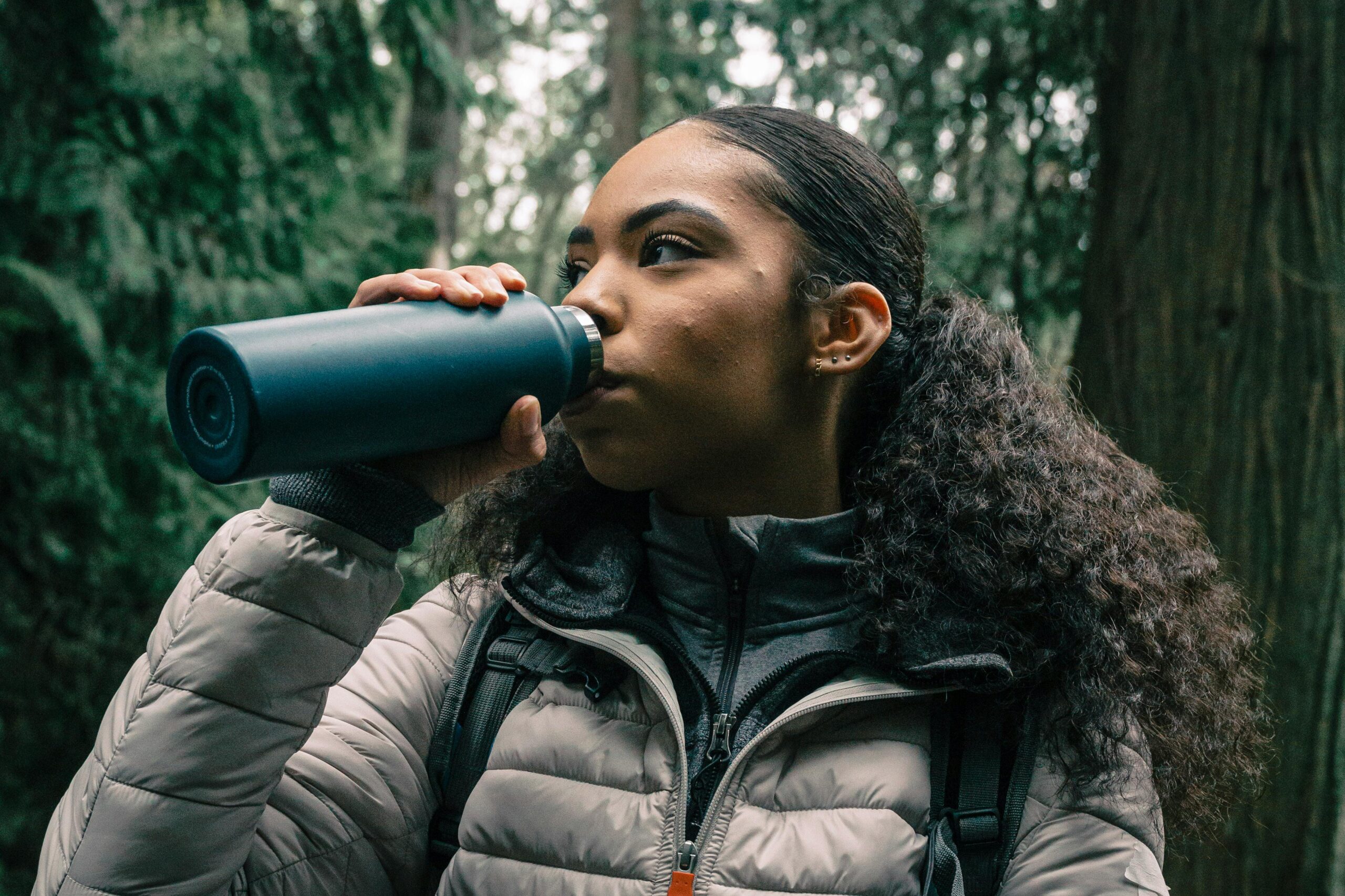 Frau trinkt im Wald aus Thermosflasche