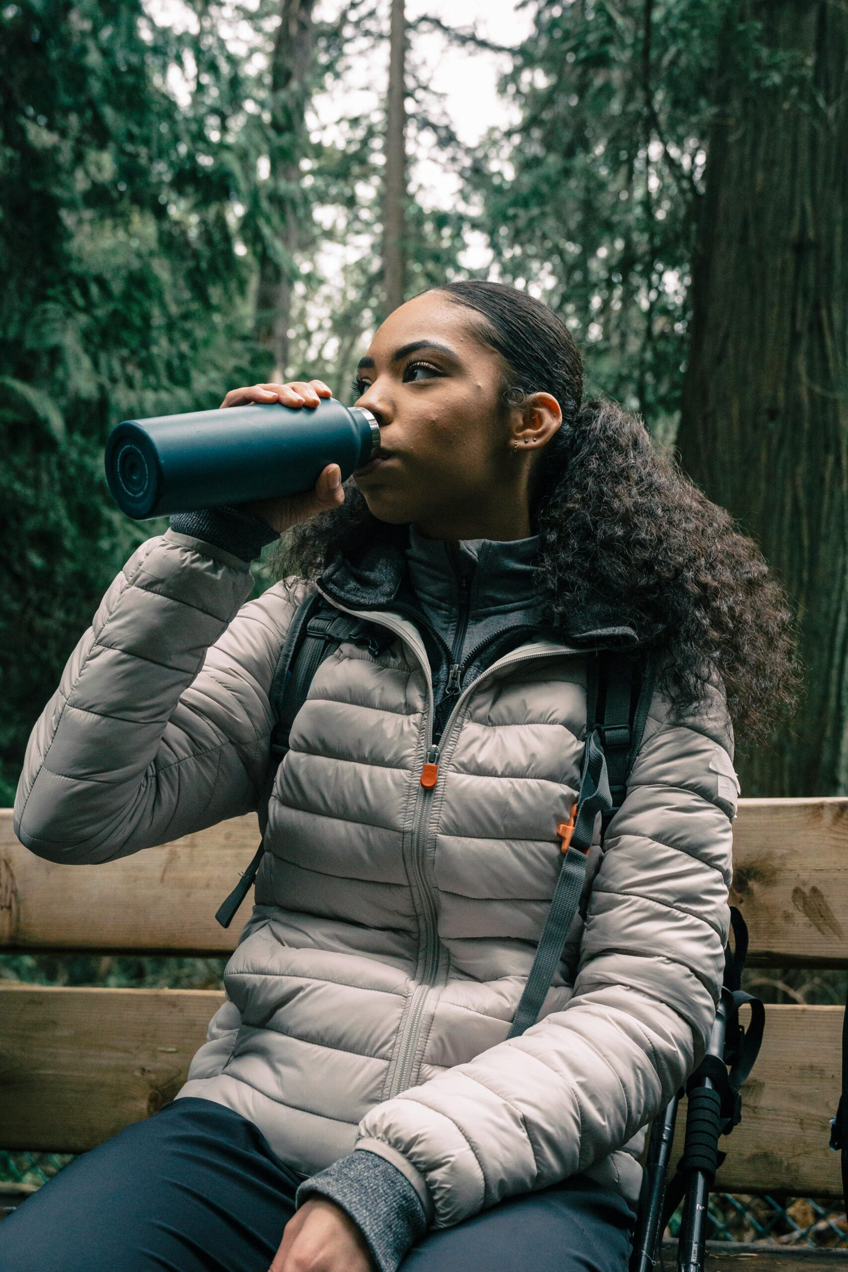 Frau sitzt im Wald und trinkt aus Trinkflasche