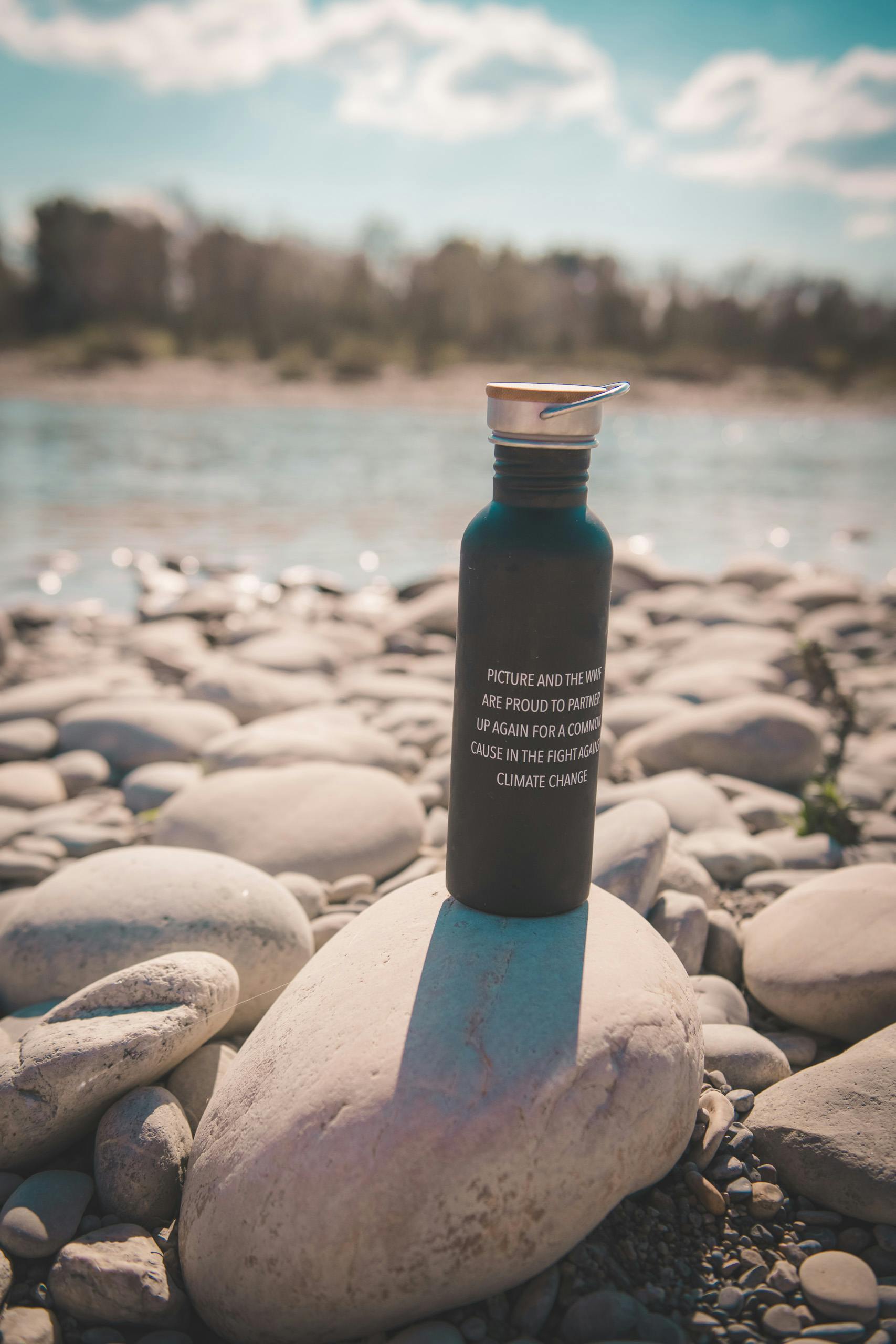 Nachhaltige Trinkflasche steht auf Steinen bei Fluss.