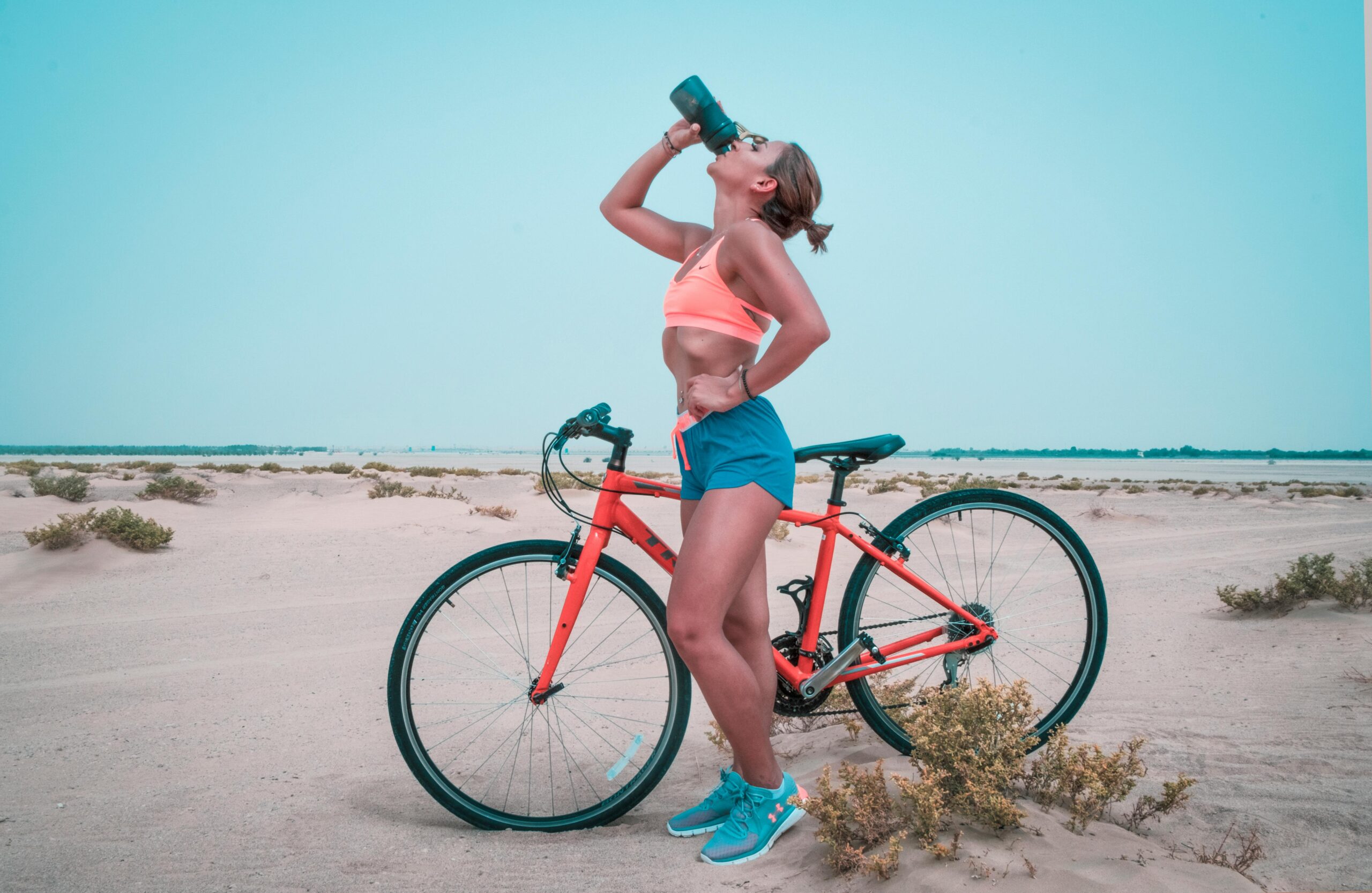 Radfahrerin trinkt am Strand aus einer Flasche